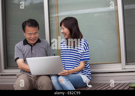 Ein Mann und eine Frau sitzen vor einem Haus. Halten einen Laptop-Computer. Stockfoto