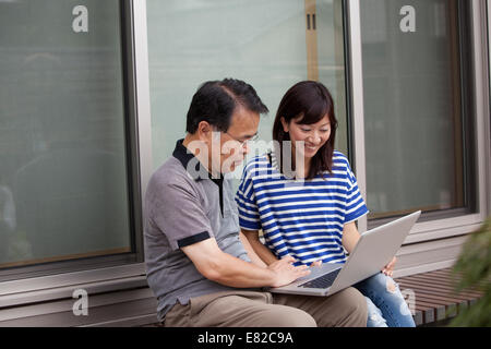 Ein Mann und eine Frau sitzen vor einem Haus. Halten einen Laptop-Computer. Stockfoto