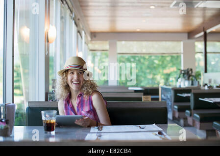 Eine Frau mit Hut sitzt in einem Diner, hält eine digitale-Tablette. Stockfoto