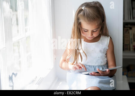 Ein junges Mädchen an einem Fensterplatz sitzen mit einem digitalen Tablet. Stockfoto