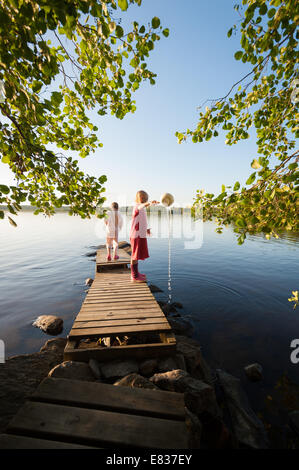 Zwei kleine Mädchen im Schlafanzug spielen mit Wasser auf einem Steg Stockfoto