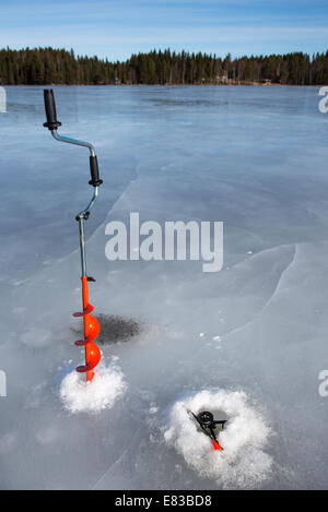 Isolierte Hand-Eisschnecke und Tip-up-Eis Angelrute am gefrorenen See im Winter, Finnland Stockfoto