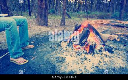 Person wärmt ihre Füße neben einem Lagerfeuer bei Abenddämmerung camping im Wald mit Instagram-Stil-filter Stockfoto