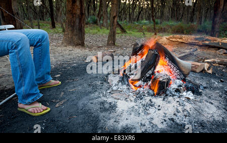 Person wärmt ihre Füße neben einem Lagerfeuer bei Abenddämmerung camping im Wald Stockfoto