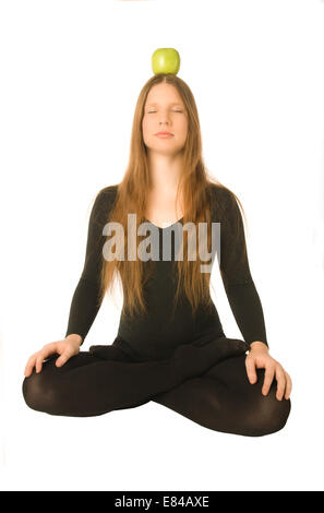 Das Porträt einer Frau in Lotus pose mit einem grünen Apfel auf dem Kopf Stockfoto