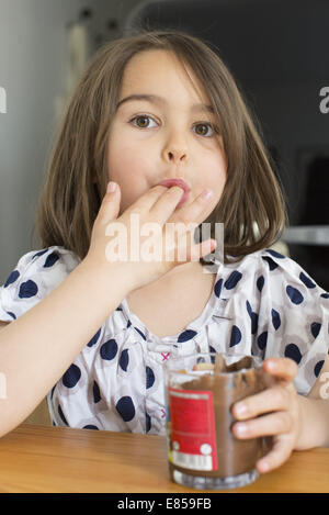 Kleines Mädchen Schokolade Soße aus dem Glas mit den Fingern essen Stockfoto