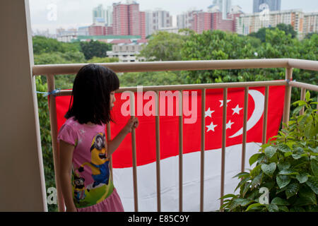 Mädchen mit Blick von einem sozialen Wohnraum HDB Immobilien und Nationalflagge in Singapur Stockfoto