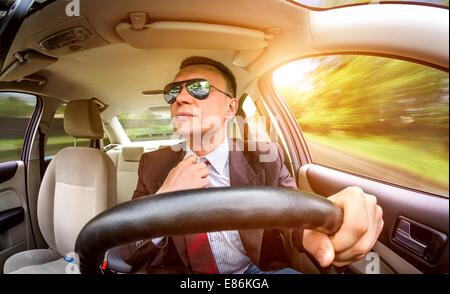 Mann in einem Anzug und Sonnenbrille auf einer Straße im Auto fahren. Stockfoto