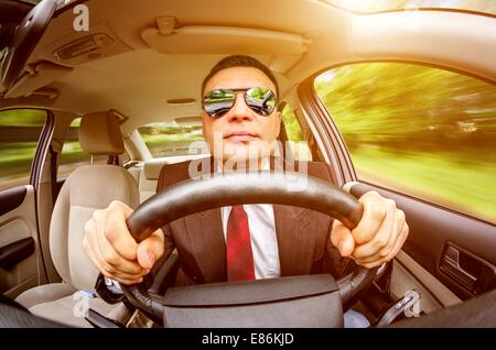 Mann in einem Anzug und Sonnenbrille auf einer Straße im Auto fahren. Stockfoto