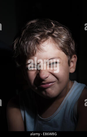 Junge in der dunklen Grimassieren, fokussiert Licht auf der einen Seite Stockfoto