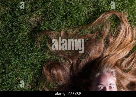 Schönes langes blondes Haar ist Sommer Rasen ausgestreut. Wir sehen nur die Hälfte des Gesichts - nur schöne Augen.  Schönes junges Mädchen liegt auf dem grünen Rasen in den Abendstunden. Stockfoto