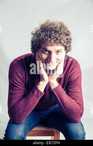 Mann weared violetten Pullover. Lockige weißer Mann im Studio sitzen Stockfoto