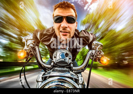 Biker Mann trägt eine Lederjacke und eine Sonnenbrille sitzt auf seinem Motorrad, Blick auf den Sonnenuntergang, Rennen auf der Straße. Filter in der Postproduktion angewendet. Stockfoto