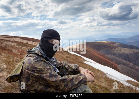 Mann mit geschlossenen Gesicht und Tarnung Kleidung sitzt auf einem Berg Stockfoto