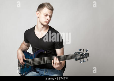 junge männliche Musiker spielt eine sechssaitige Bassgitarre auf hellem Hintergrund isoliert Stockfoto