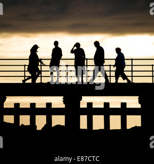 5 fünf Passanten in der Silhouette, zu Fuß am Steg Anlegestelle deck an einem Sommer Abend Aberystwyth Wales UK Stockfoto