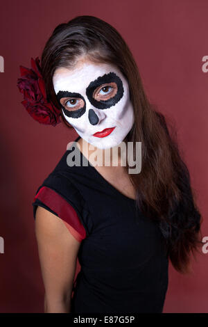 Frau mit Make-up von la Santa Muerte mit roten Rosen vor einem roten Hintergrund Stockfoto