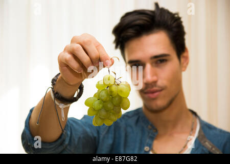Junger Mann hält eine große leckere reifere Reihe von Trauben baumelt an seiner Hand, den Fokus auf die Frucht Stockfoto