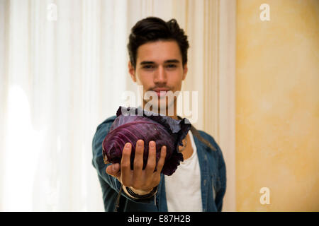 Lächelnde junge Mann einen frischen schwarzen Kohl in seiner Hand hält, in einer gesunden Ernährung und Lebensstil oder vegetarisch-Konzept Stockfoto