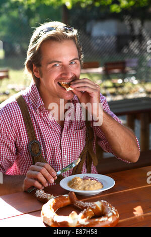 Attraktiver kaukasischer Mann isst traditionelle Käse mit Brezel in einem bayerischen Biergarten Stockfoto