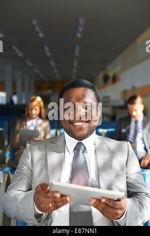 Young African-American Geschäftsmann mit Touchpad Blick in die Kamera mit zwei Kollegen auf Hintergrund Stockfoto