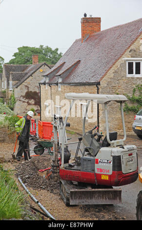 Ein Arbeiter installiert neue Glasfaser-Breitbandkabel in einem malerischen Dorf in Süd-England Stockfoto