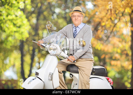 Ältere Gentleman posiert auf einem Roller in einem Park an einem schönen Tag Stockfoto