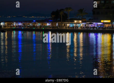 Nachtleben Cala Estancia mit Neonröhren über die kleine Bucht und Neonlicht Reflexionen von den Restaurants. In der Ferne Stockfoto