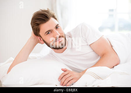 Hübscher junger Mann im weißen Bett Stockfoto