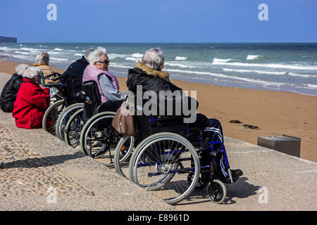 Gruppe der älteren Menschen im Rollstuhl am Strand beobachten das Wasser an einem kalten Tag entlang der Nordseeküste Stockfoto