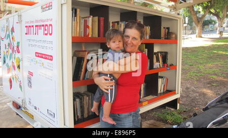 Tel Aviv, Israel. 1. Oktober 2014. Eva Milrad steht vor einem Bücherregal in der Mitte des belebten Rothschild Boulevard im Zentrum von Tel Aviv, Israel, 1. Oktober 2014. Der 56-jährige glaces über den Buchrücken, aufgereiht in einer öffentlichen "Lesung Box." "Ich komme oft hierher und nehmen Sie Bücher," sagt die freundliche Frau im roten T-shirt, die unterwegs mit ihrem einjährigen Enkel ist. Zwei neue Straße Bibliotheken wurden in die israelische Kunsthauptstadt Tel Aviv in dieser Woche eröffnet. Das bringt die insgesamt acht in der ganzen Stadt. Foto Sara Lemel/Dpa/Alamy Live News Stockfoto