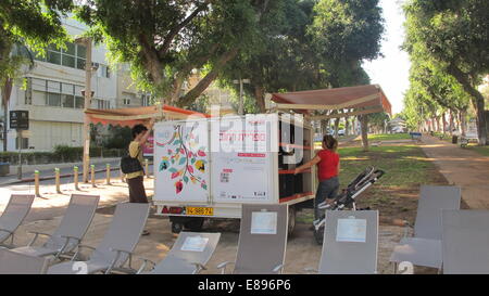 Tel Aviv, Israel. 1. Oktober 2014. Eva Milrad steht vor einem Bücherregal in der Mitte des belebten Rothschild Boulevard im Zentrum von Tel Aviv, Israel, 1. Oktober 2014. Der 56-jährige glaces über den Buchrücken, aufgereiht in einer öffentlichen "Lesung Box." "Ich komme oft hierher und nehmen Sie Bücher," sagt die freundliche Frau im roten T-shirt, die unterwegs mit ihrem einjährigen Enkel ist. Zwei neue Straße Bibliotheken wurden in die israelische Kunsthauptstadt Tel Aviv in dieser Woche eröffnet. Das bringt die insgesamt acht in der ganzen Stadt. Foto Sara Lemel/Dpa/Alamy Live News Stockfoto