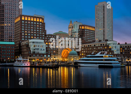 Boston Harbor mit Skyline im Finanzdistrikt als Hintergrund während der Dämmerung Stunde. Das Custom House Clock Tower können gesehen werden beleuchtet sowie Rowes Wharf, der Odyssee Kreuzfahrt Yacht, die Samuel Clemens Replik steamship zusammen mit anderen Hochhäusern entlang der Uferpromenade. Auch als Schwarz und Weiß zu drucken. Stockfoto