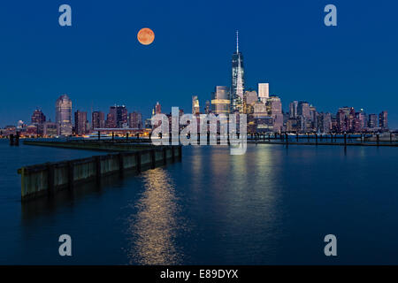 Der super Mondaufgang über den beleuchteten Wolkenkratzern in der unteren Manhattan Skyline entlang One World Trade Center. Stockfoto