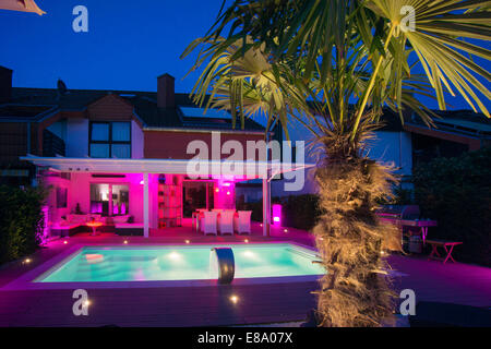 Private Reihenhaus mit Wintergarten, einen Pool, eine Terrasse und eine Palme mit Displaybeleuchtung in der Nacht, Deutschland Stockfoto