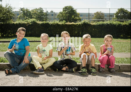 Kinder mit Tassen zusammensitzen am Bordstein Stockfoto