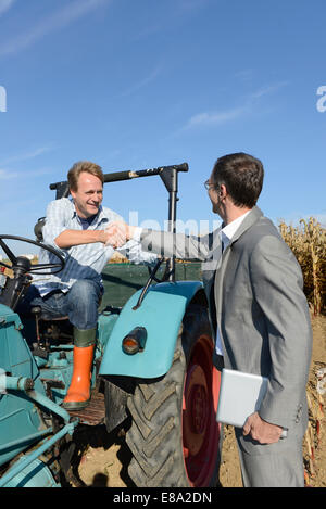 Landwirt begrüßt Geschäftsmann mit Handschlag, beim Sitzen auf einem Traktor im Kornfeld, Bayern, Deutschland Stockfoto