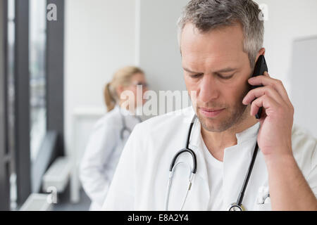 Arzt am Telefon während Ärztin im Hintergrund Stockfoto