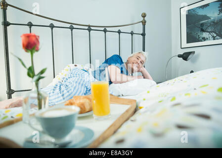 Frühstückstablett auf Bett während reifer Mann im Hintergrund Stockfoto