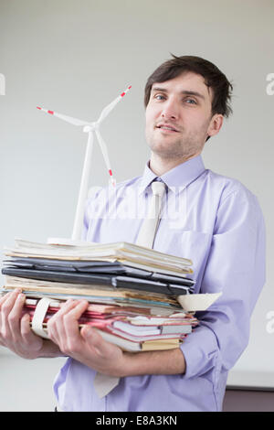 Porträt der Geschäftsmann Stapel von Dateien und Modell-Windmühle in Büro, hält lächelnd Stockfoto