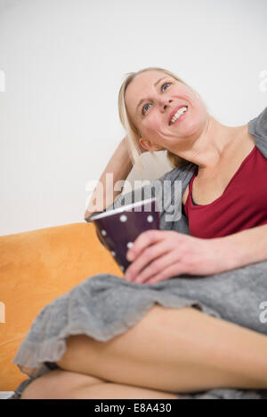 Entspannen Sie sich auf der Couch mit Tasse, Reife Frau lächelnd Stockfoto