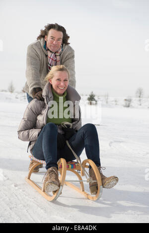 Mann drängen Frau auf Schlitten im Schnee, Bayern, Deutschland Stockfoto