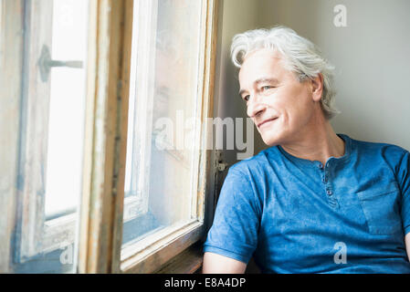 Reifer Mann sitzt vor Fenster, Lächeln Stockfoto