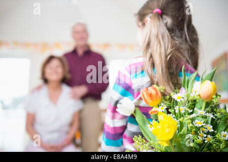 Enkelin Übergabe Blumenstrauß zu Großmutter und Großvater im Hintergrund Stockfoto