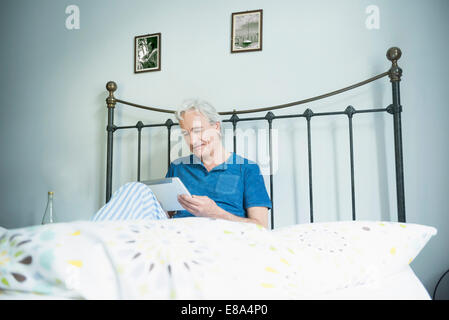 Reifer Mann im Bett sitzen und mit digital-Tablette, Lächeln Stockfoto