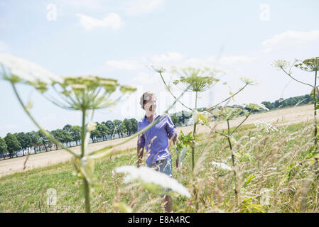 Mitte erwachsenen Mann zu Fuß in Wiese mit Blumen, Lächeln Stockfoto