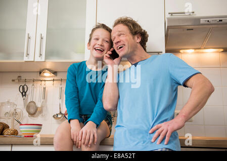 Lachen, Vater und Sohn mit Handy in Küche Stockfoto