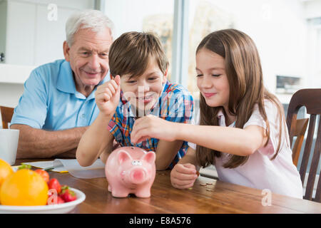 Zwei Kindern und Großvater mit Sparschwein Stockfoto