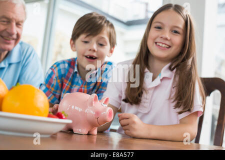 Zwei glückliche Kinder und Großvater mit Sparschwein Stockfoto