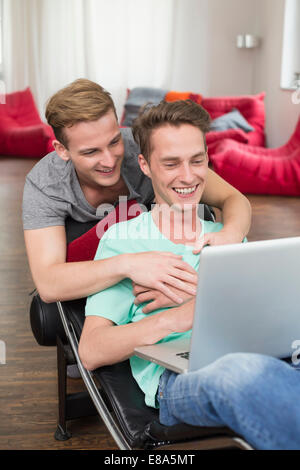 Homosexuelles Paar mit Laptop im Liegestuhl, Lächeln Stockfoto